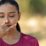 Woman pinching nose outdoors, eyes closed