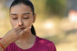 Woman pinching nose outdoors, eyes closed