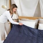 Woman arranging a weighted blanket on bed.