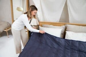 Woman arranging a weighted blanket on bed.